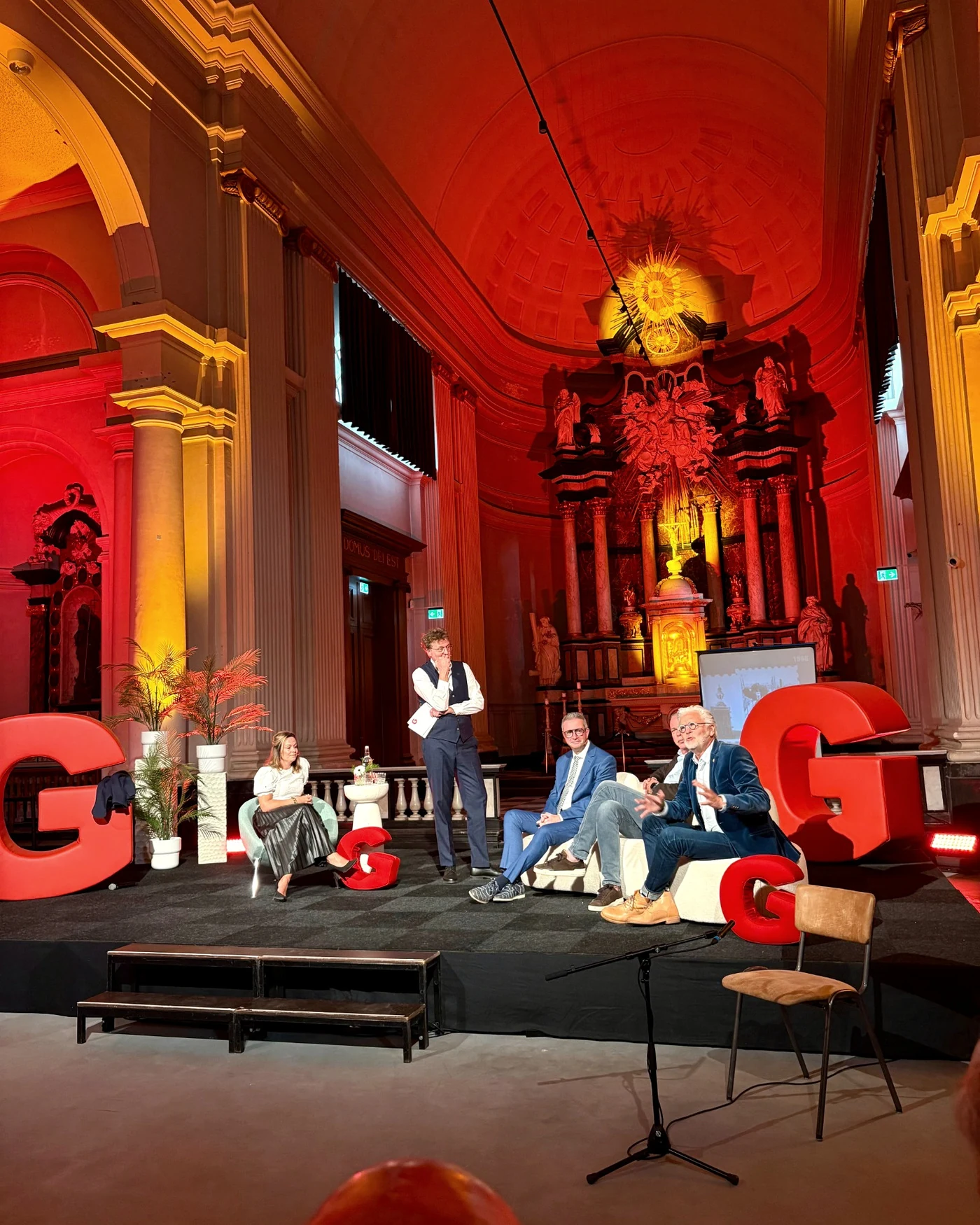 Programmering in de Sint-Jan: een panelgesprek op het podium in rood en geel aangelicht kerkinterieur
